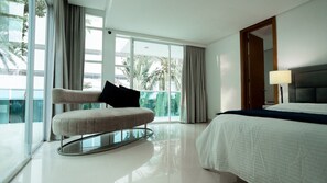 A modern hotel room with a large bed, a sofa with a pillow, a nightstand, and a view of palm trees through large windows. - Luxury Cartagena villa near beach- VIP amenities, airport pickups, 24/7 staff (Cartagena de Indias)