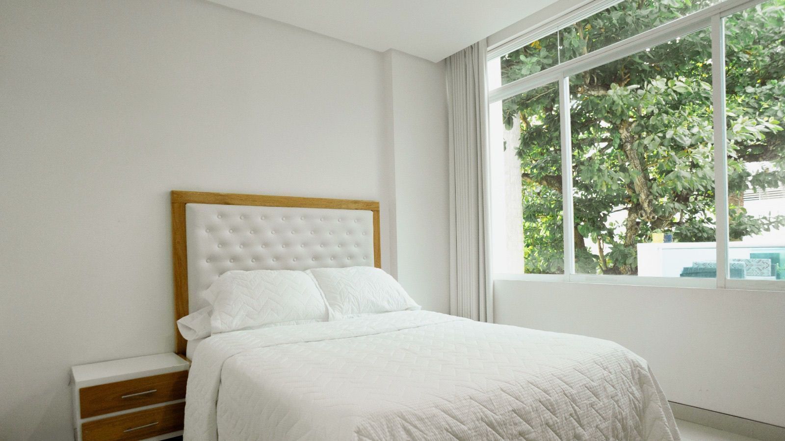 A bedroom with a bed, a wooden nightstand, and a window with curtains.