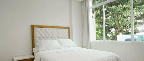 A bedroom with a bed, a wooden nightstand, and a window with curtains.