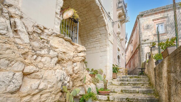 Un escalier étroit en pierre, dans un bâtiment historique, agrémenté de plantes en pot et doté d’un espace extérieur aménagé pour s’asseoir.