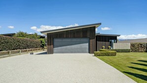 A modern building with a large garage door, a gravel driveway, and well-maintained landscaping. - Diamond on the Peninsula (Wānaka)