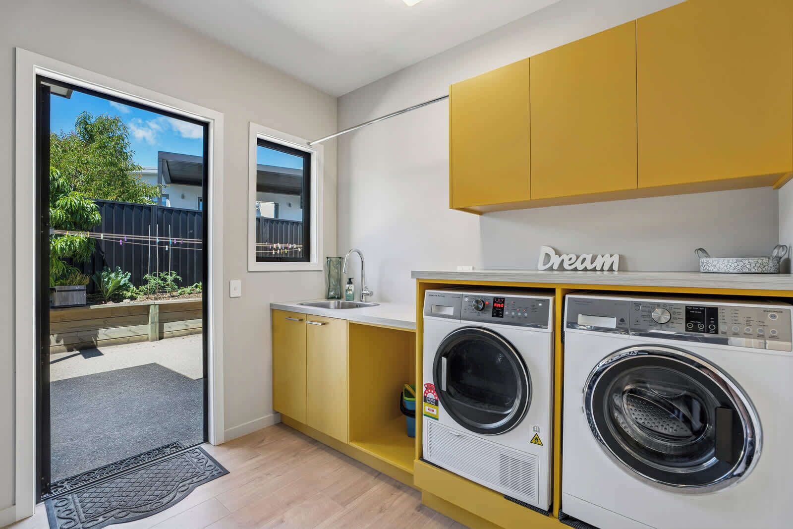 A compact kitchen with two washing machines, a sink, and a window overlooking a garden.