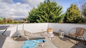 Une terrasse sur le toit, avec des chaises longues, une petite table et un fauteuil en osier.