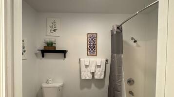 A bathroom with a toilet, a shower, and a bathtub. There are two towels hanging on the wall.