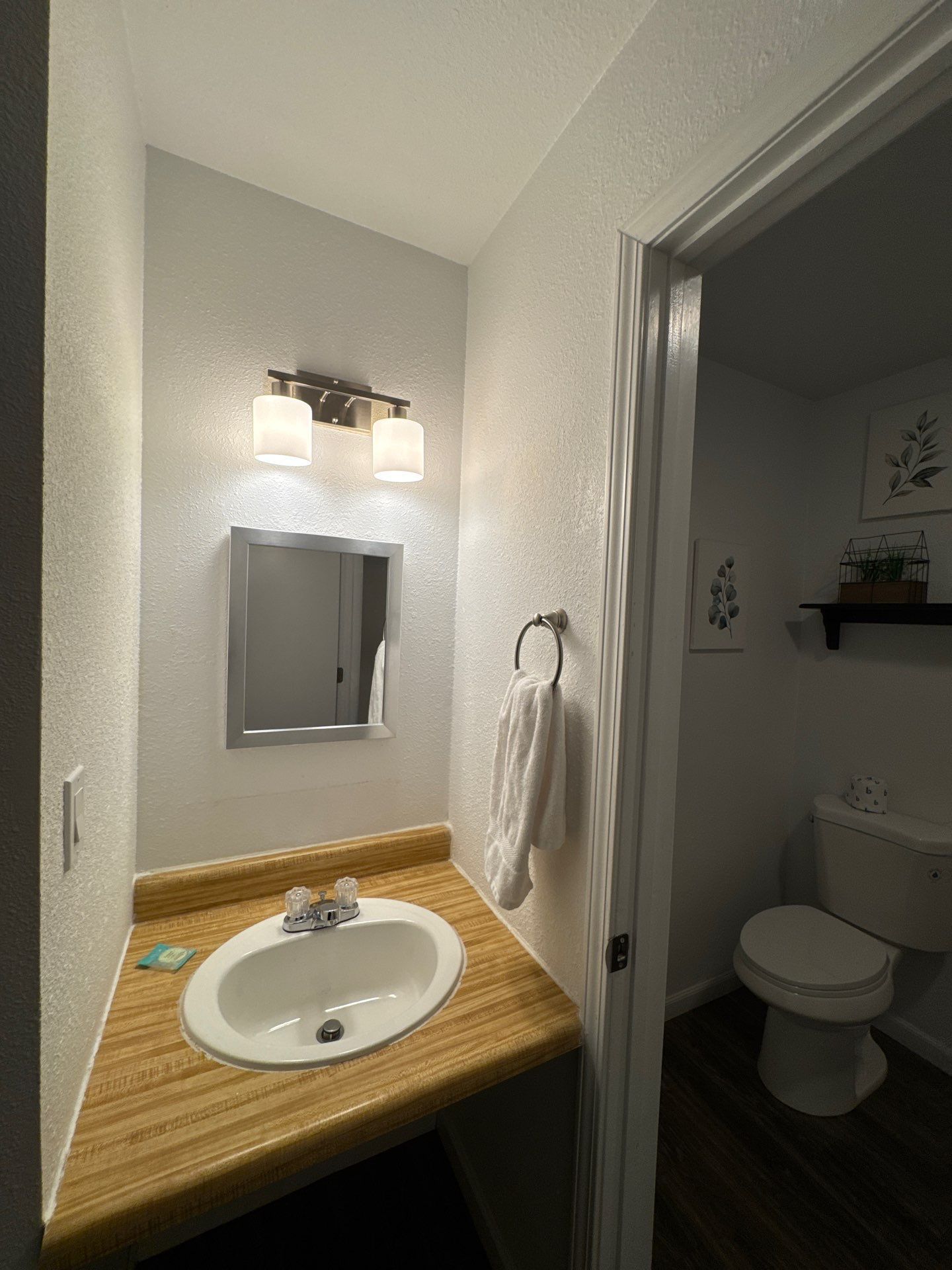 A bathroom with a wooden vanity, a white sink, a mirror, and a toilet.