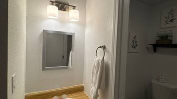 A bathroom with a wooden vanity, a white sink, a mirror, and a toilet.