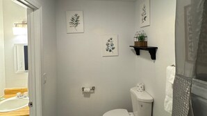 Een kleine badkamer met toilet, een klein plankje met een plantje, en twee aan de muur hangende foto's.