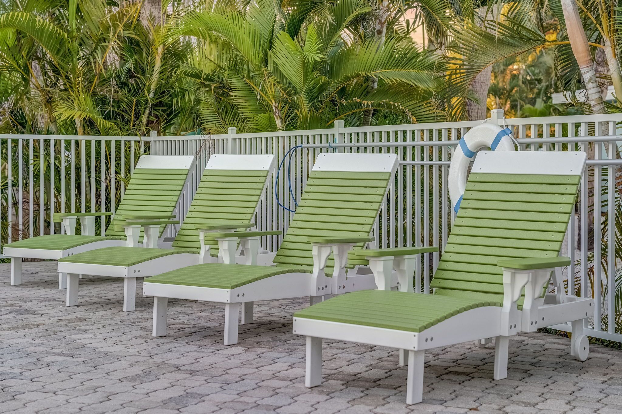 Une rangée de chaises longues vertes et blanches, avec une rambarde blanche en arri ère-plan.