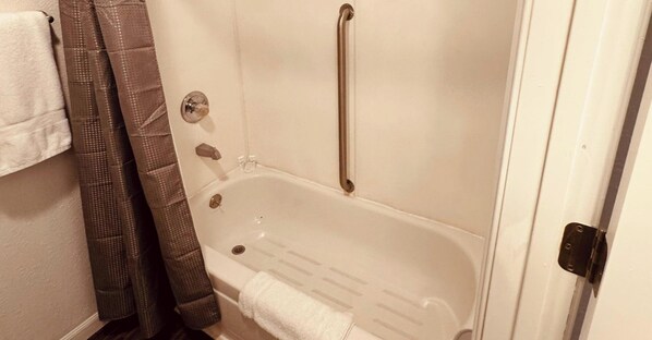 A bathroom with a white bathtub, a shower curtain, and a towel rack. - Wedding and Party Venue (Challenge-Brownsville)
