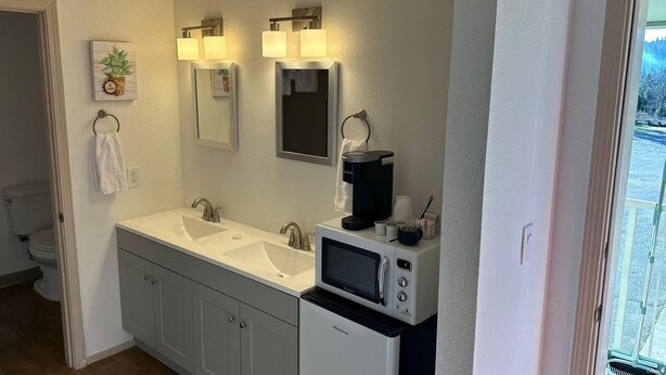 A bathroom with a double sink, a toilet, a mirror, and a coffee maker. - Wedding and Party Venue (Challenge-Brownsville)