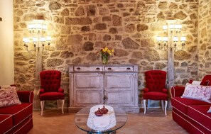 A room with a stone wall, two red armchairs, a glass coffee table with a lace tablecloth, and a wooden cabinet with a vase of flowers. - Amazing home in Vicchio di Mugello with sauna (Vicchio di Mugello)