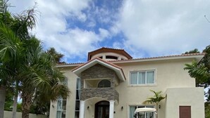 A two-story house with a stone facade, a balcony, and a driveway with a golf cart. - The Crown Oasis Luxury Escape All Inclusive (Puerto Plata)