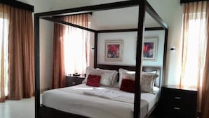 A four-poster bed with a dark frame, white bedding, and decorative pillows. There are two nightstands with lamps, and a painting on the wall above the bed. - The Crown Oasis Luxury Escape All Inclusive (Puerto Plata)