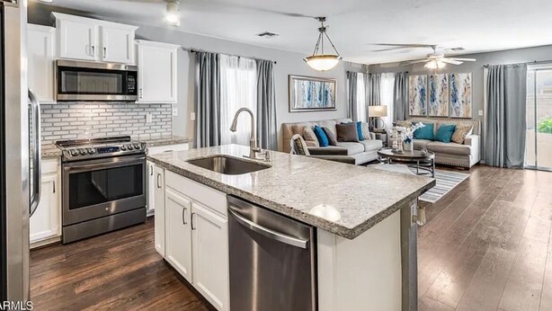 A modern kitchen with white cabinets, a granite countertop, stainless steel appliances, and a central island with a sink. - Spacious 4BR w/ Backyard Spa Near Westgate Az (Youngtown)