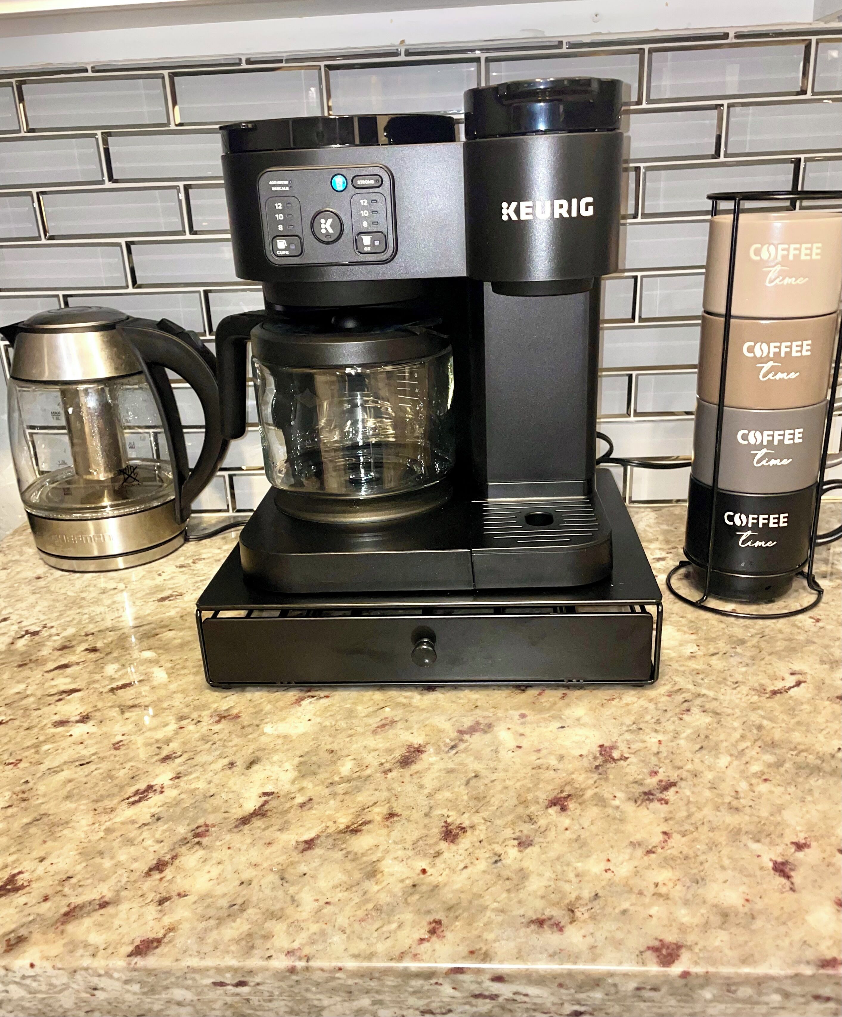 Eine Keurig-Kaffeemaschine auf einer Küchenarbeitsplatte, zusammen mit einer weiteren Kaffeemaschine und einer Glaskaraffe.