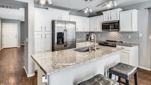 A modern kitchen with white cabinets, granite countertops, stainless steel appliances, and pendant lighting. - Spacious 4BR w/ Backyard Spa Near Westgate Az (Youngtown)