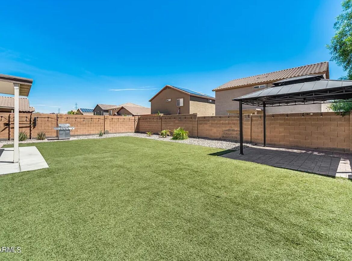 Un jardin arrière d’une maison, avec une pelouse bien entretenue, un mur en briques et une terrasse couverte.