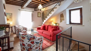 A cozy living room with a red sofa, floral armchair, and a glass coffee table. A staircase with a wooden railing leads to an upper level. - Gorgeous apartment in Frazione Canonica,Todi (Frazione Canonica,Todi)