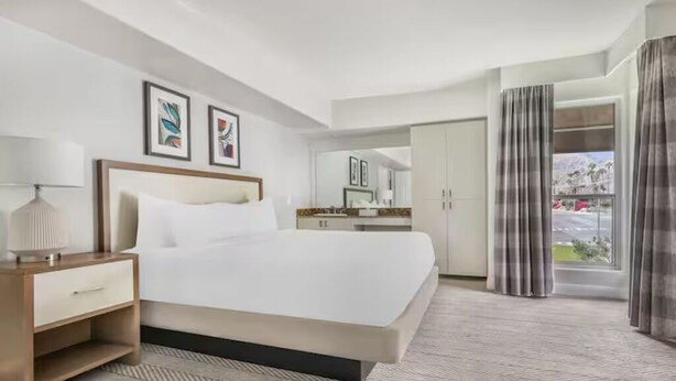 Hotellihuone, jossa on suuri sänky, yöpöytä ja liukuoven kautta avautuva näkymä ulos.