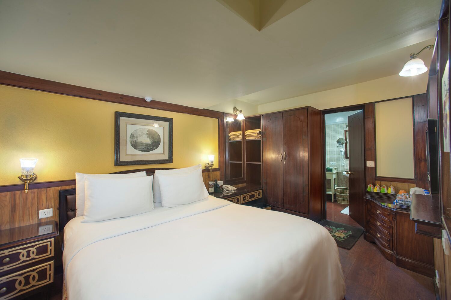 Une chambre d’hôtel avec un grand lit, une armoire en bois et un tableau encadré au mur.