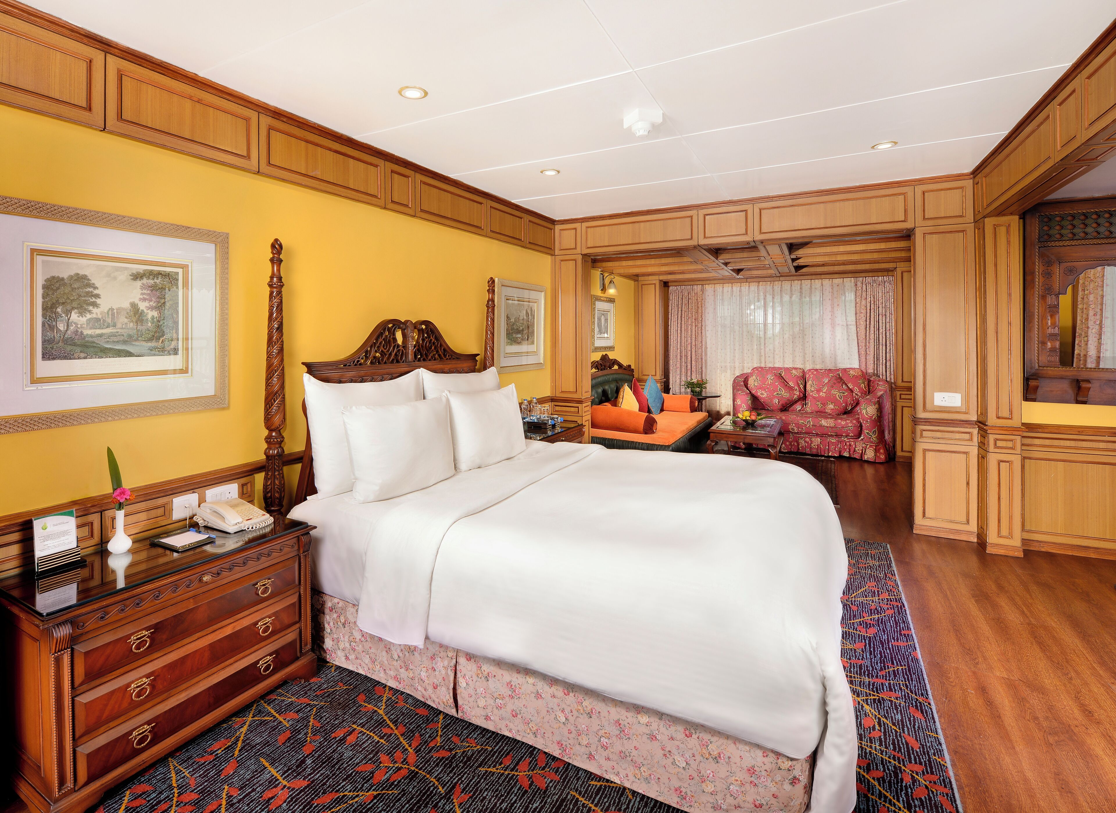 Une chambre d’hôtel avec un grand lit, une commode en bois, un bureau avec un téléphone et un canapé rouge.