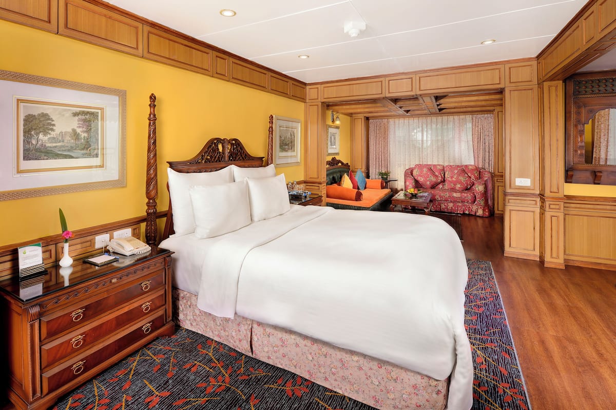 Een hotelkamer met een groot bed, een houten dressoir, een bureau met telefoon en een rode bank.