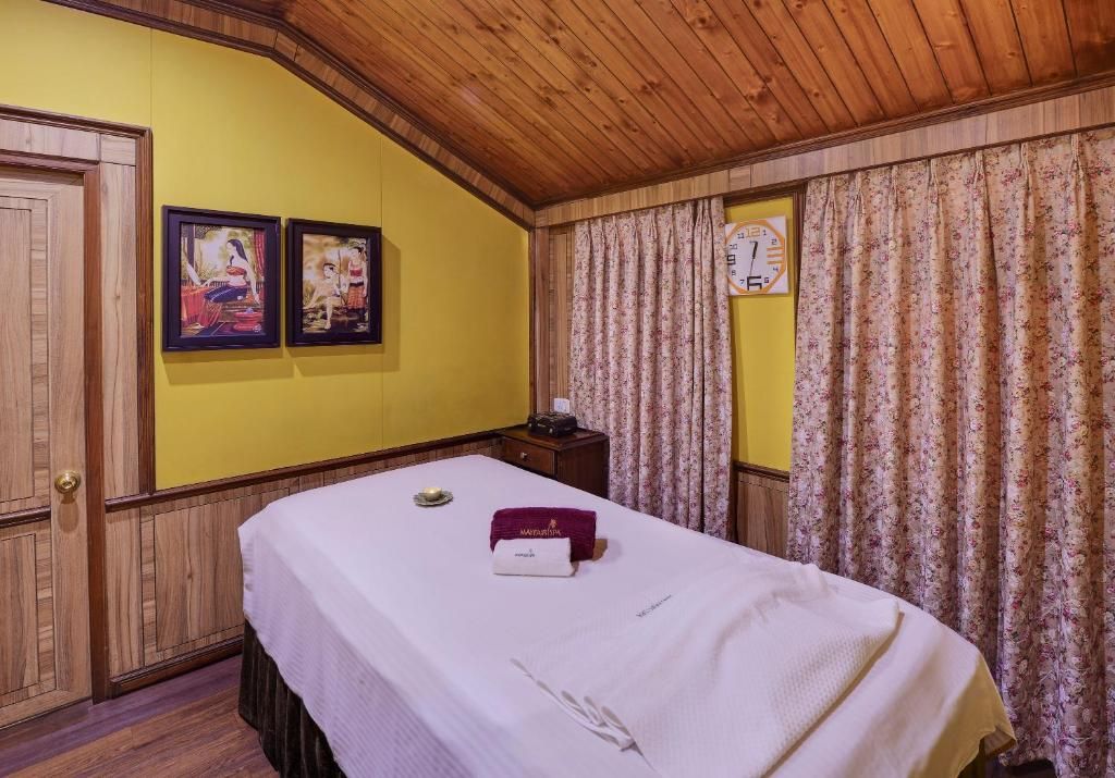 A hotel room with a wooden ceiling, yellow walls, a bed with a white bedspread, a small nightstand, and two framed pictures on the wall.