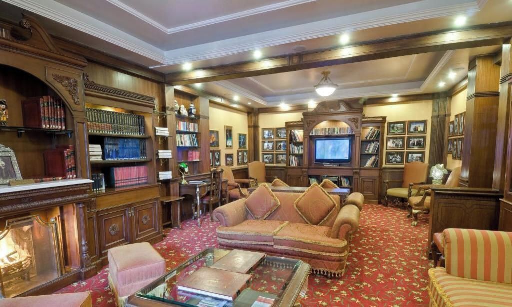 A traditional library with bookshelves, a sofa, a television, and framed pictures.