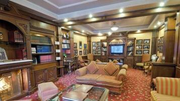 A traditional library with bookshelves, a sofa, a television, and framed pictures.