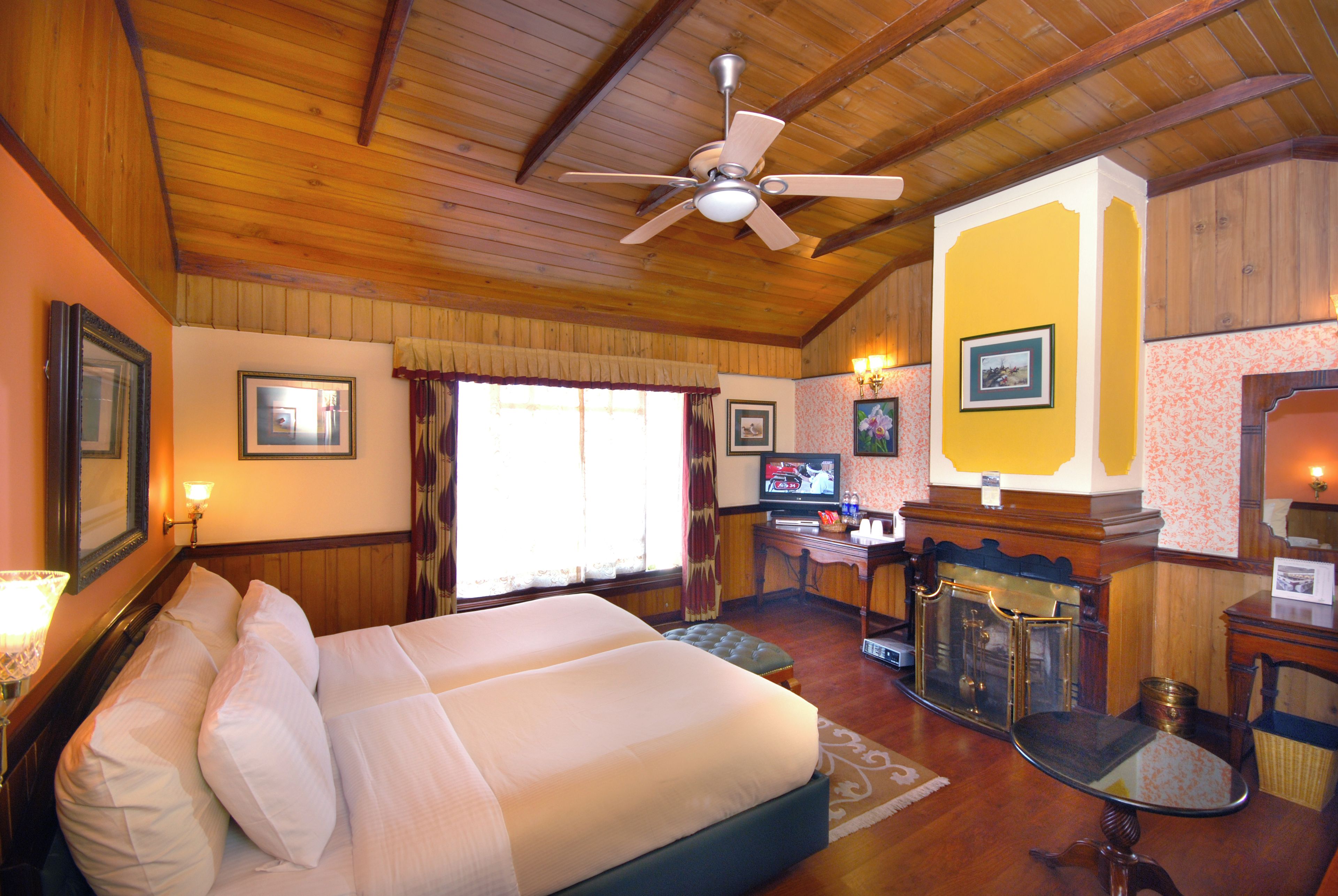 Una habitación de hotel con una cama grande, ventilador de techo, escritorio con televisor y chimenea.