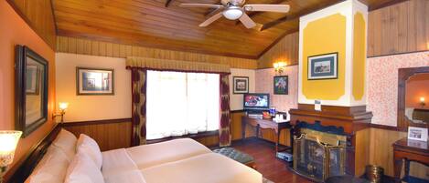 Una habitación de hotel con una cama grande, ventilador de techo, escritorio con televisor y chimenea.