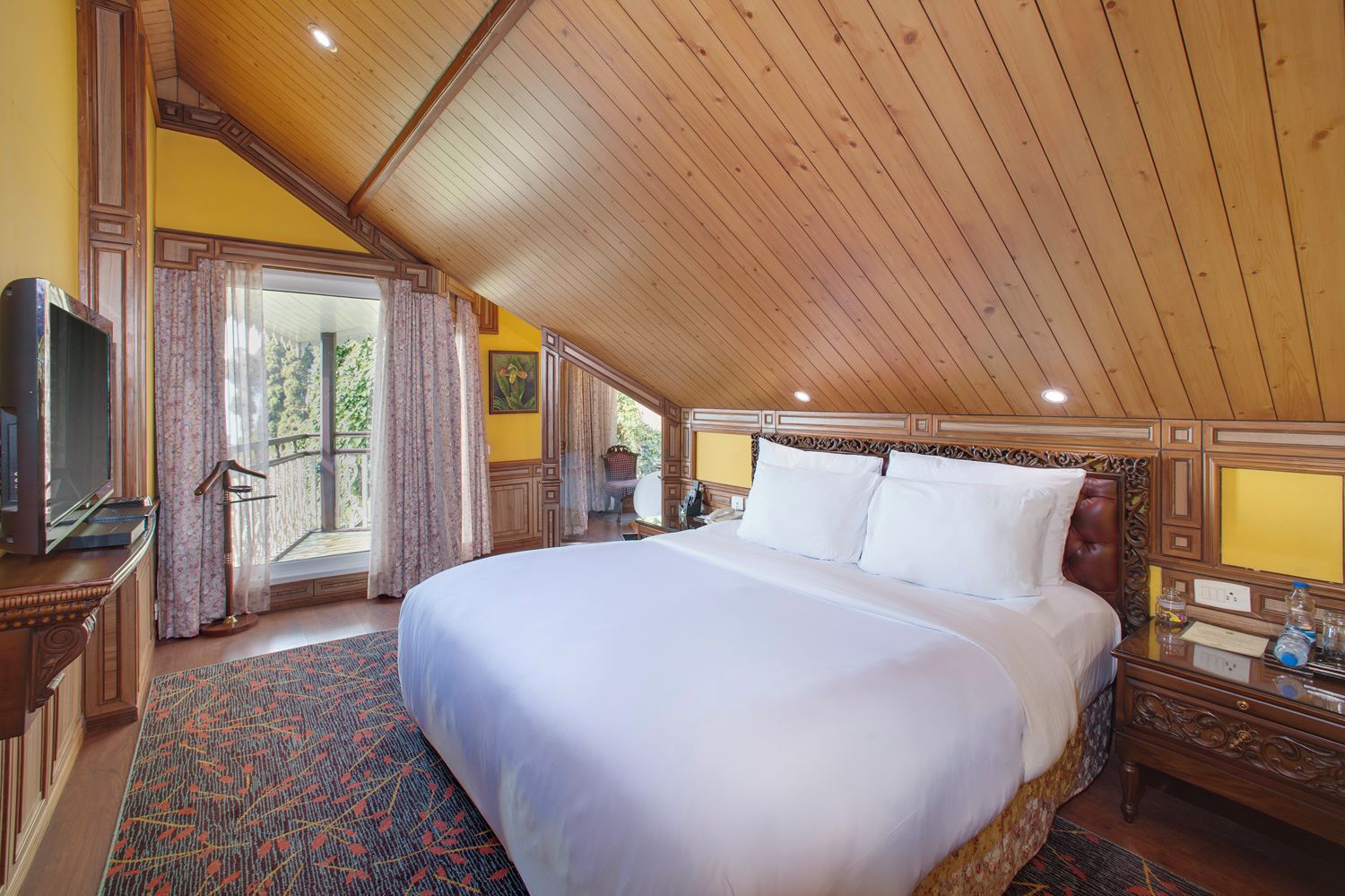 A spacious bedroom with a large bed, wooden ceiling, and a balcony with curtains.