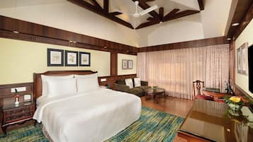 A hotel room with a large bed, a wooden headboard, a desk with a vase, a chair, and a ceiling fan.