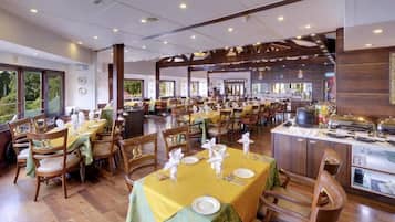 A spacious dining area with multiple tables set for guests, featuring a central island with a coffee machine and a view of the outdoors.