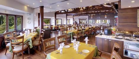A spacious dining area with multiple tables set for guests, featuring a central island with a coffee machine and a view of the outdoors.