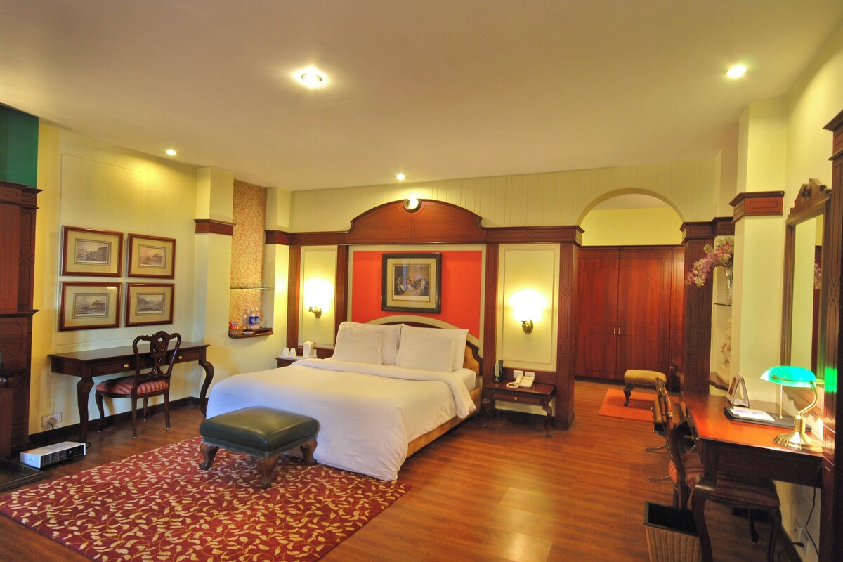 Quarto de hotel com uma cama grande, uma escrivaninha, uma cadeira, uma luminária de mesa e um telefone.