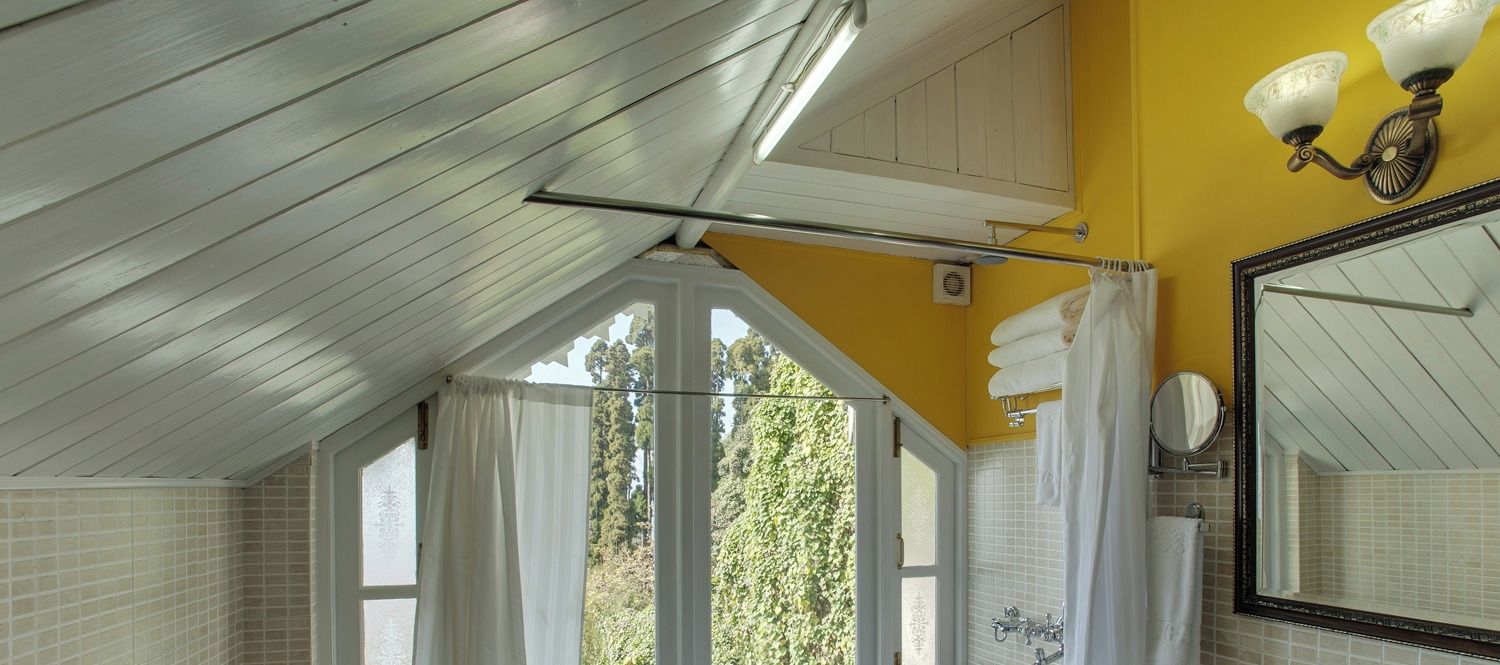 A bathroom with a sloped ceiling, a large mirror, and a window with curtains.