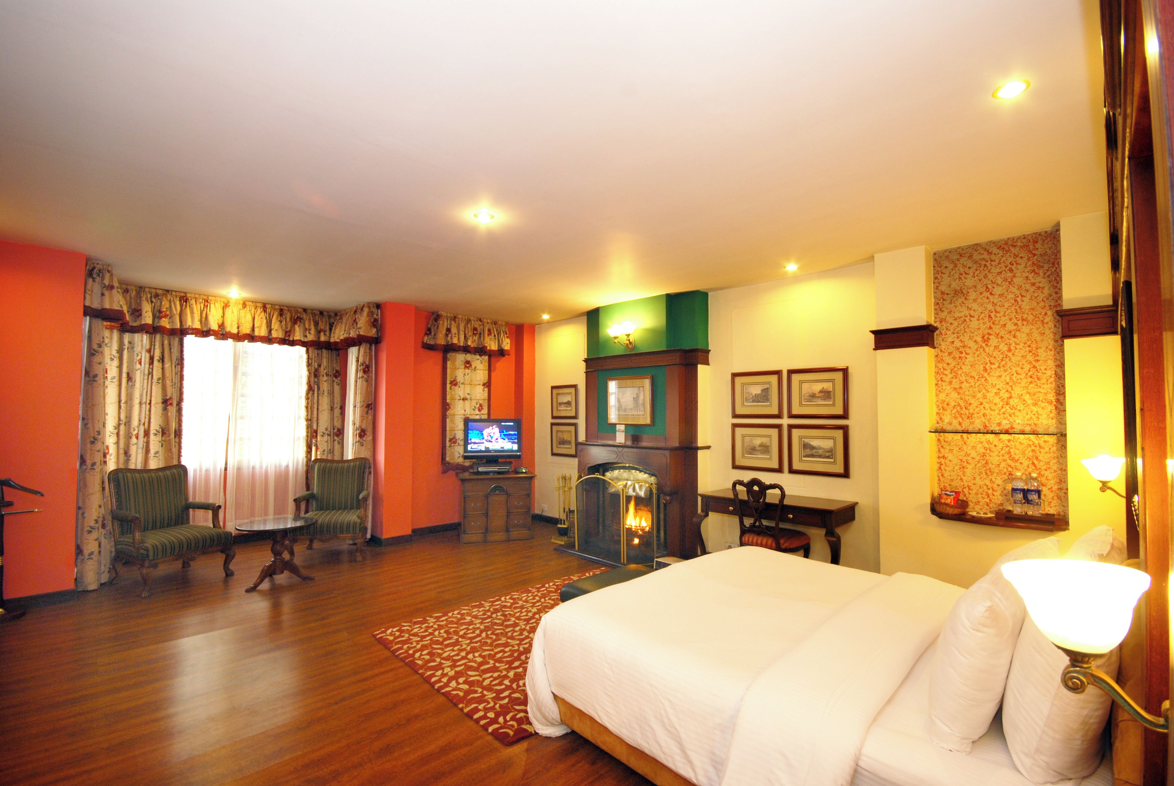 A hotel room with a large bed, a television, a fireplace, and two armchairs.