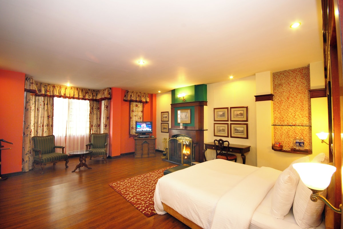 Una habitación de hotel con una cama grande, televisión, chimenea y dos sillones.