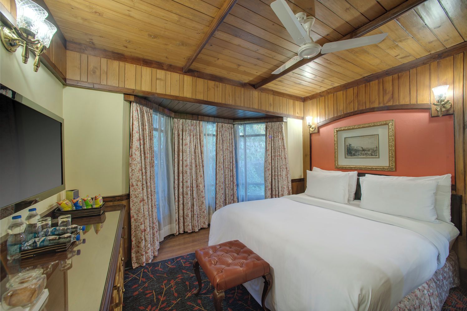 A hotel room with a bed, a desk with toiletries, a ceiling fan, and a window with curtains.