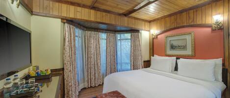 A hotel room with a bed, a desk with toiletries, a ceiling fan, and a window with curtains.