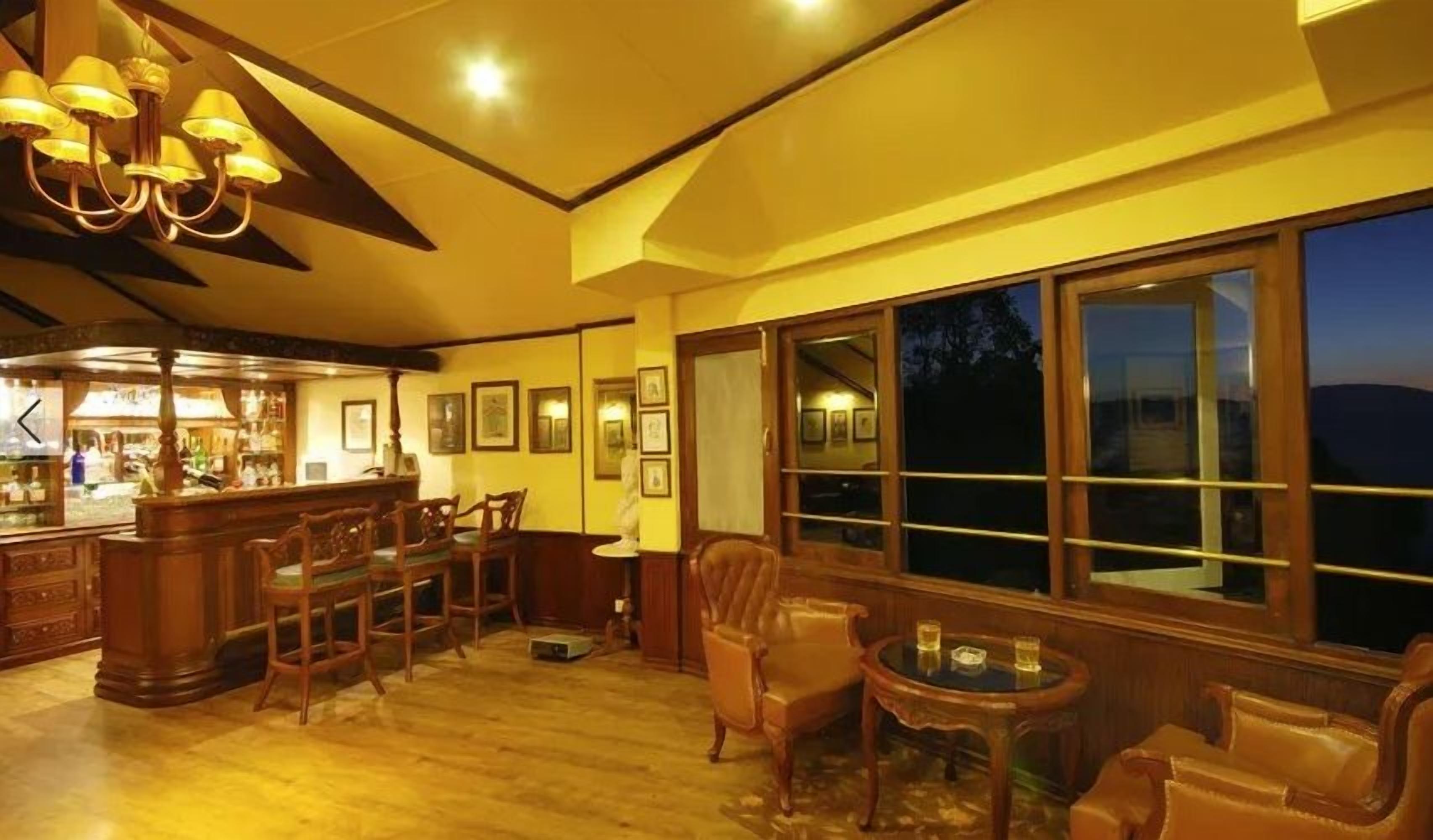 A warmly lit bar area with wooden furniture and large windows overlooking a night scene.