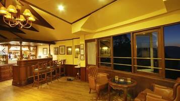 A warmly lit bar area with wooden furniture and large windows overlooking a night scene.