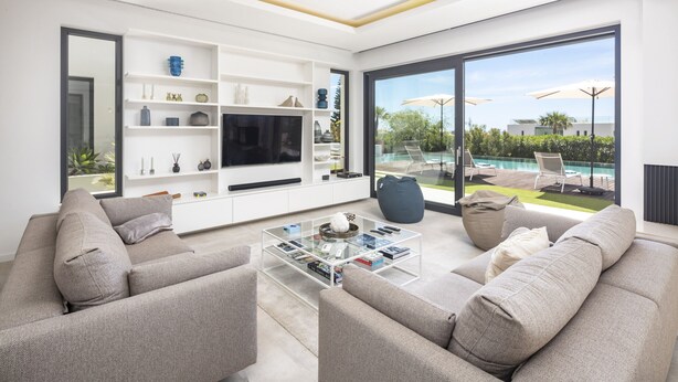 Ein modernes Wohnzimmer mit Sofa, Couchtisch, Fernseher und Regalen.