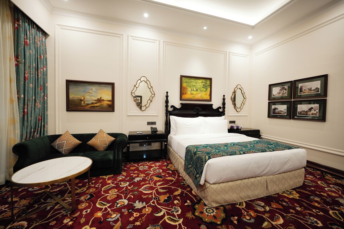 Una habitación de hotel con una cama, un sofá, una mesa redonda y suelo alfombrado.