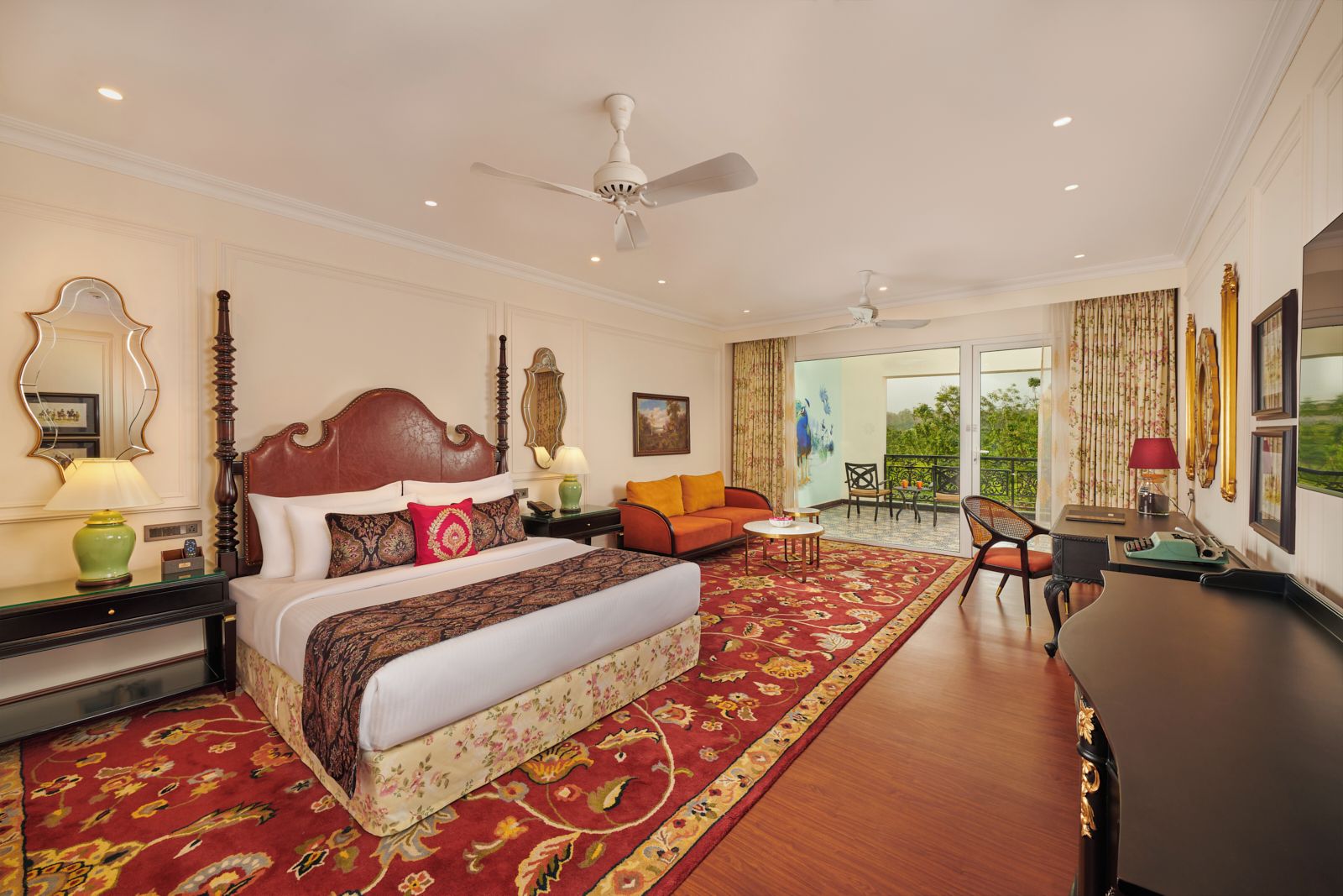 A spacious hotel room with a large bed, a sitting area with a sofa and chairs, a desk, and a balcony with a view.