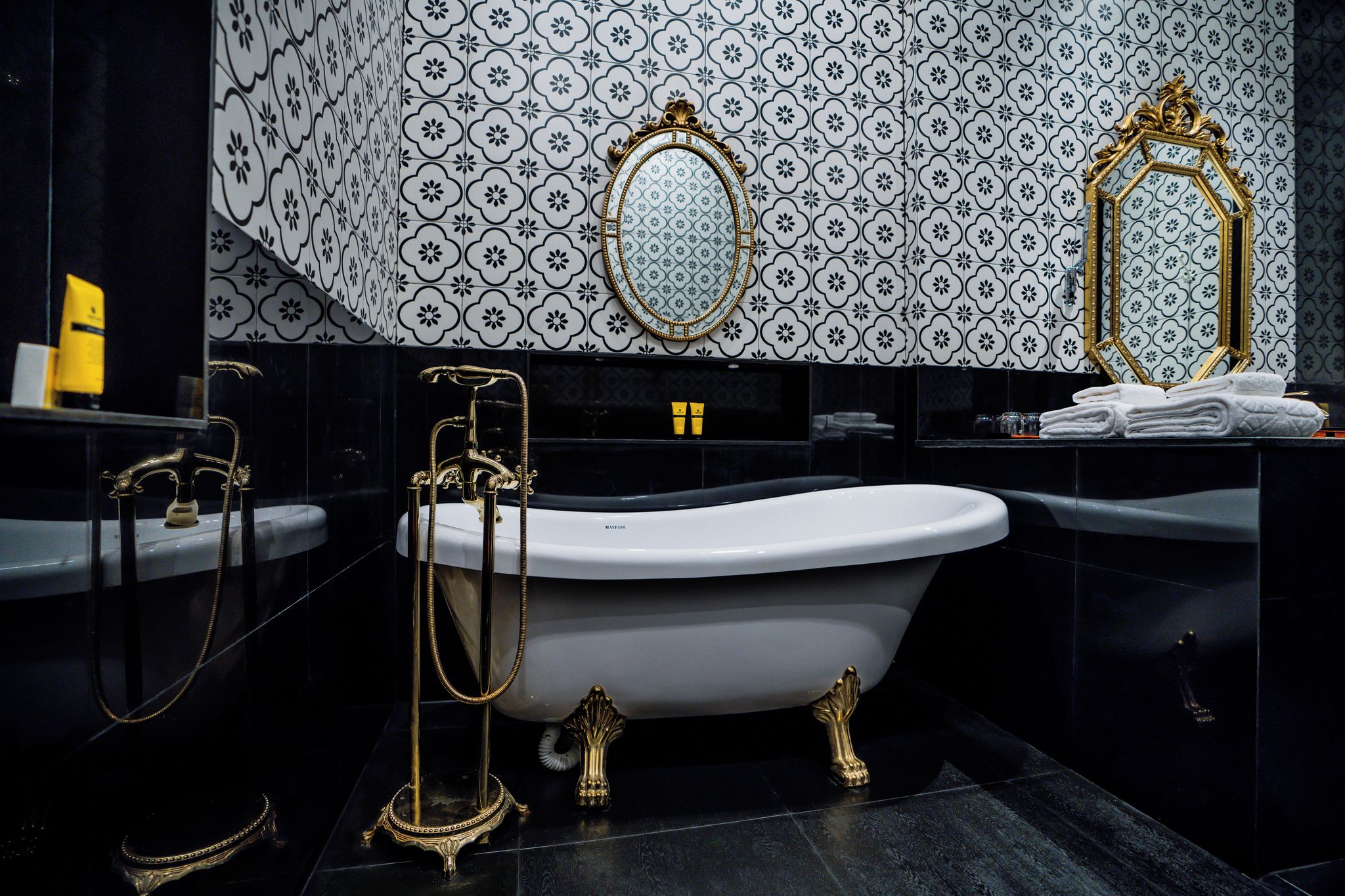 Une salle de bain avec une baignoire sur pieds, deux miroirs encadrés de doré et un mur recouvert de carreaux à motifs.