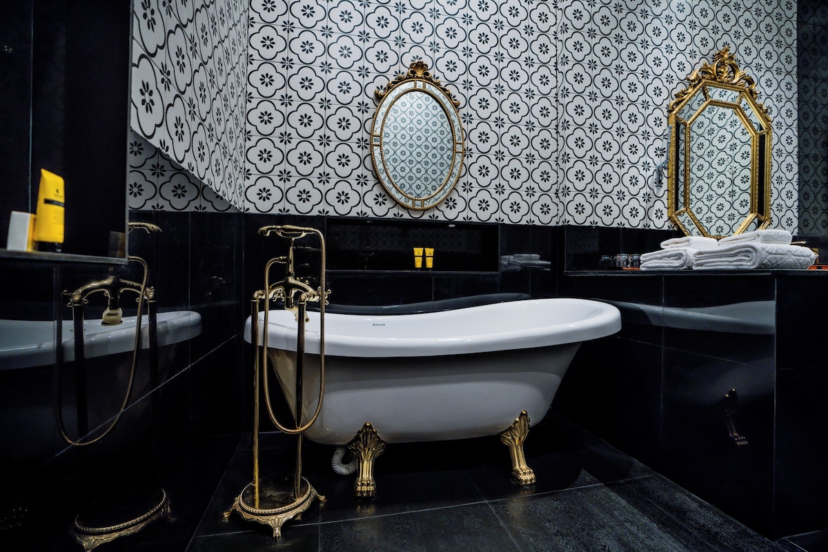 A bathroom with a freestanding bathtub, two gold-framed mirrors, and a patterned tile wall.