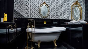Une salle de bain avec une baignoire sur pieds, deux miroirs encadrés de doré et un mur recouvert de carreaux à motifs.