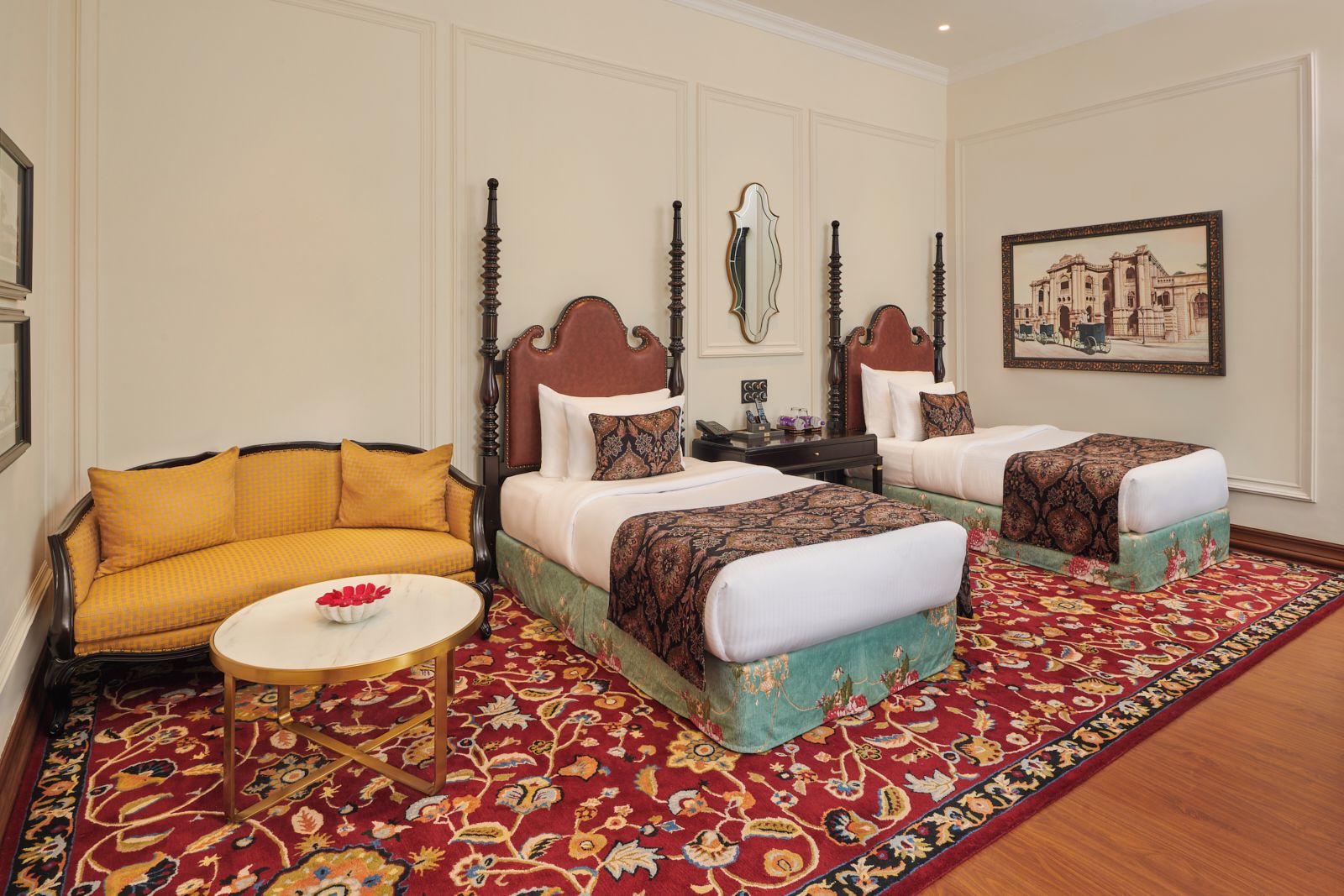 Une chambre d’hôtel avec deux lits, un canapé, une petite table ronde et un tapis à motifs.